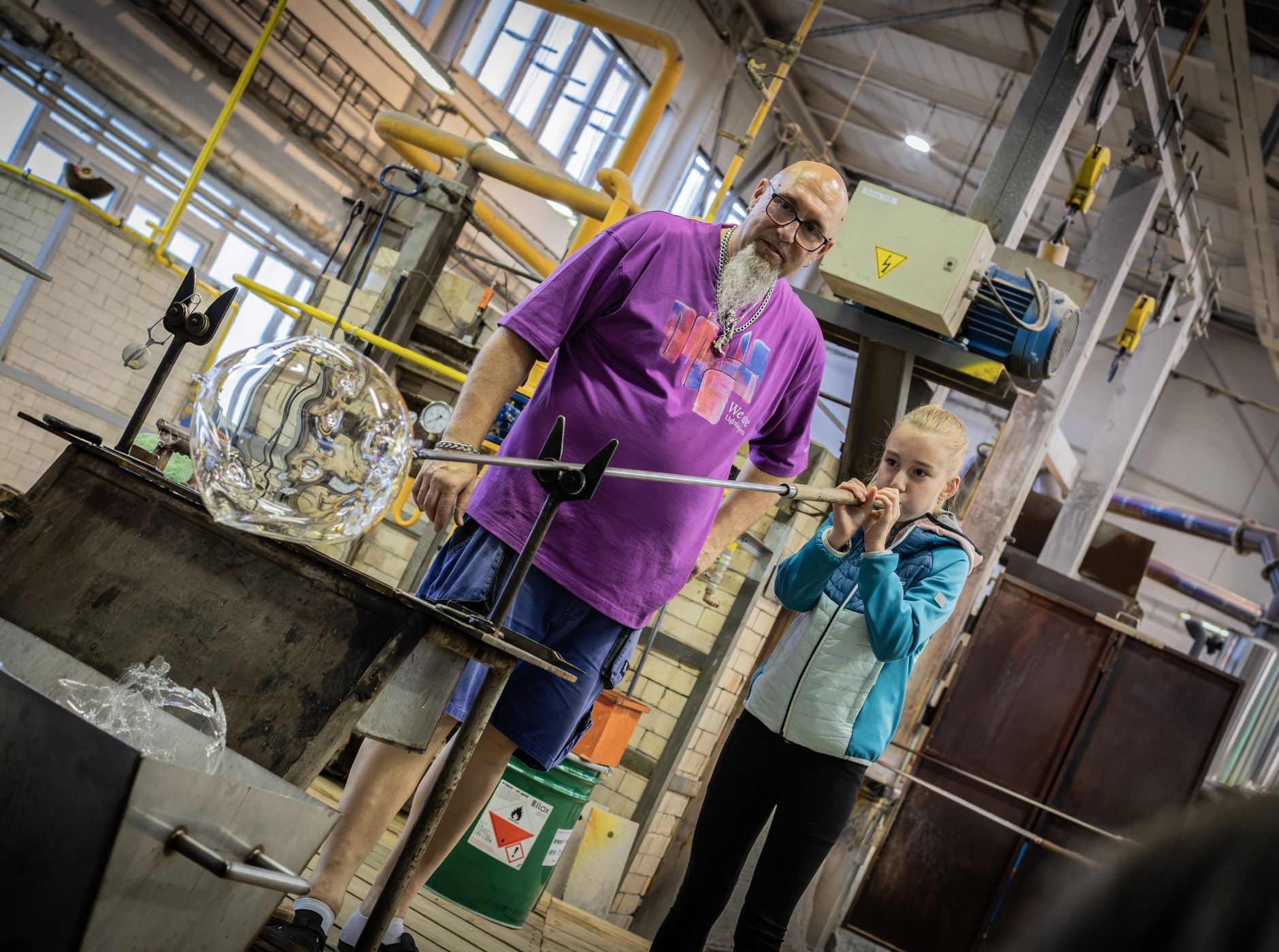 A glassmaster demonstrates blowing glass to a young participant during the Open Day event.