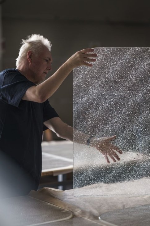 An artist handling a transparent sheet with fine bubbles in a bright studio.