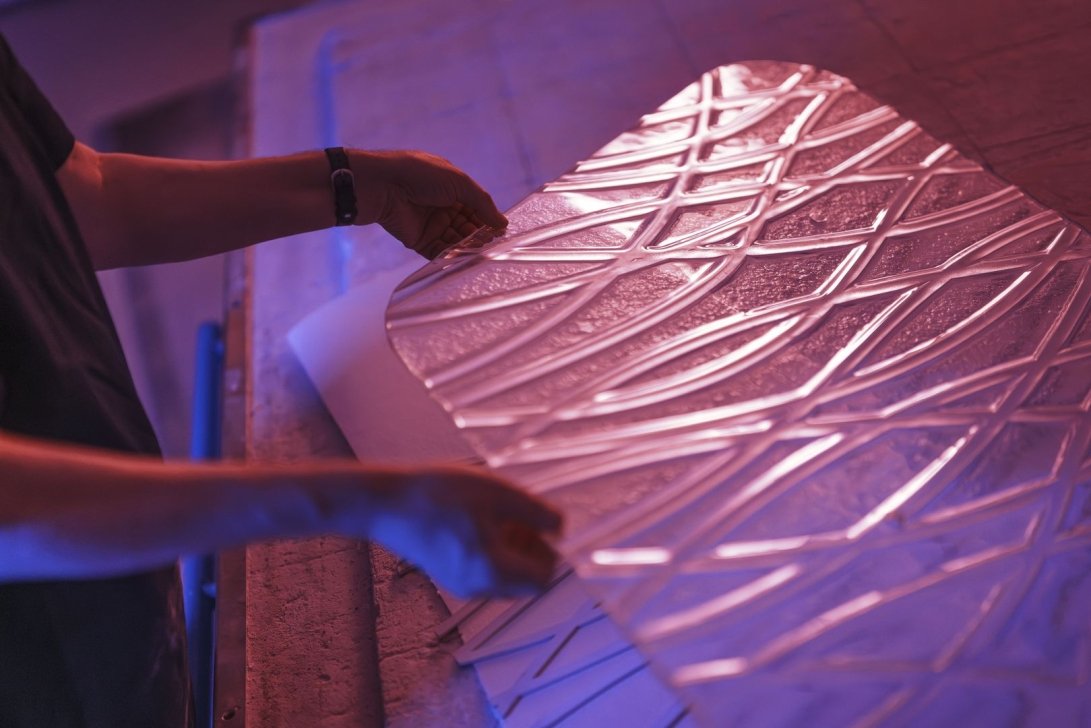 Hands handling a textured acrylic sheet under blue lighting.