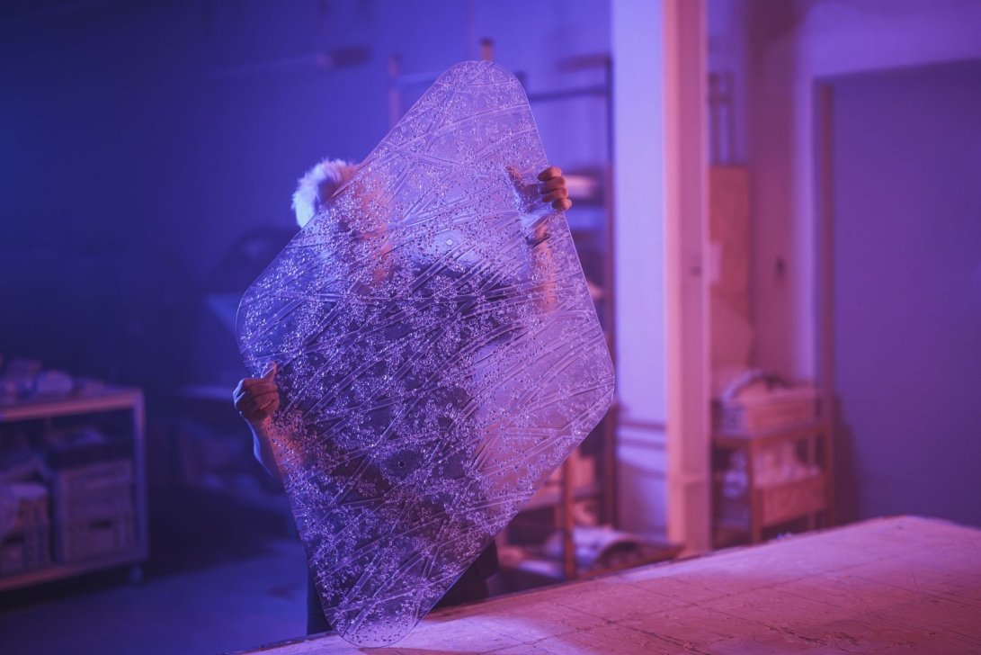A person holding a large decorative plastic panel in unusual lighting.