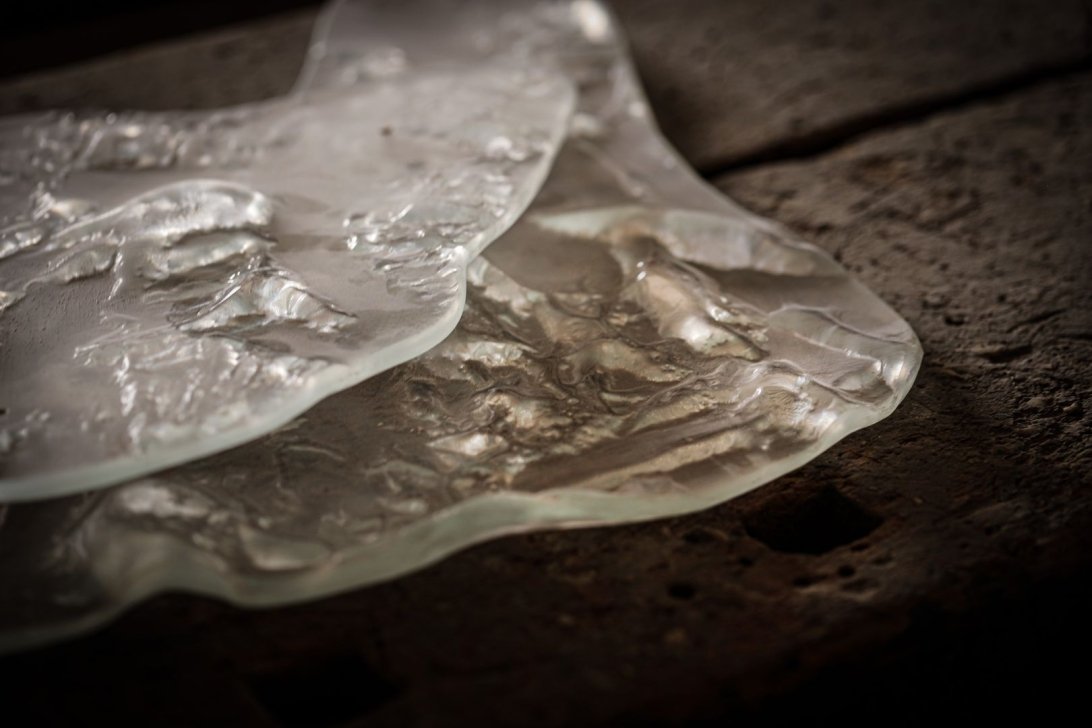 Various shapes and textures of glass sheets on a wooden surface.