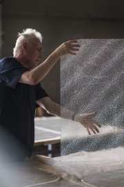 An artist handling a transparent sheet with fine bubbles in a bright studio.