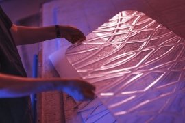 Hands handling a textured acrylic sheet under blue lighting.