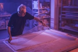 Man handling a large glass panel in a dimly lit workshop.