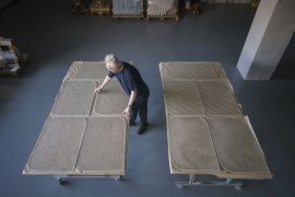 An artist creates sand textures on large paper sheets.