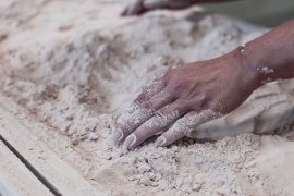 A hand covered in flour shapes dough on a work surface.